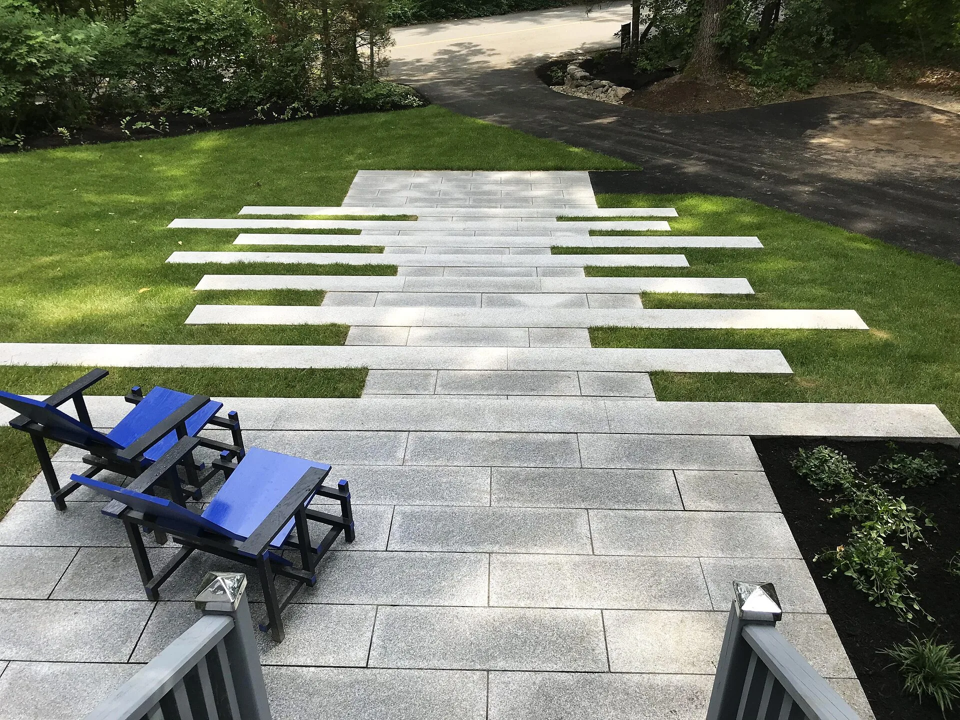 Granite plank walkway set into lawn leading to a paver patio with blue and black chairs