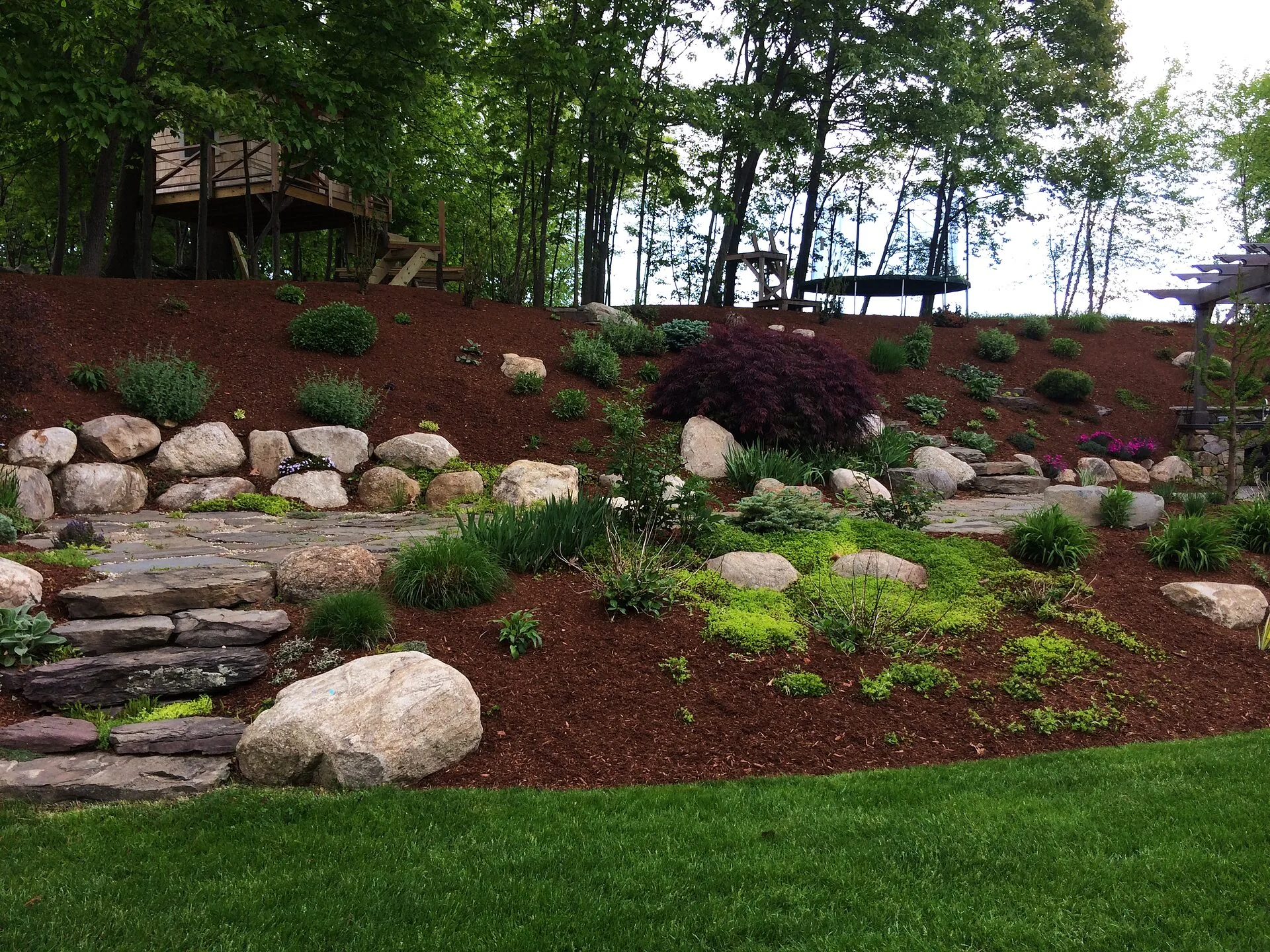 Terraced hillside with boulder walls, stone steps and mulched planting beds above a mowed lawn