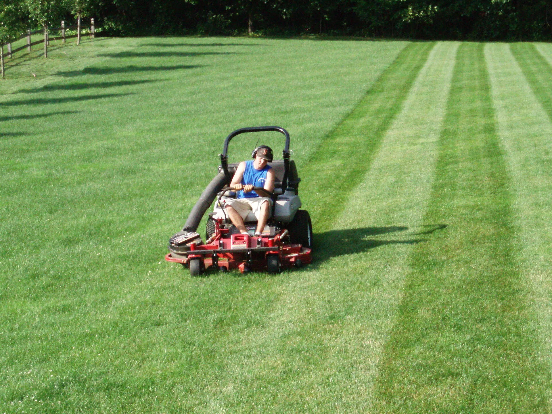 Man wearing ear protection riding a red zero turn mower across a large lawn with striped mowing lines
